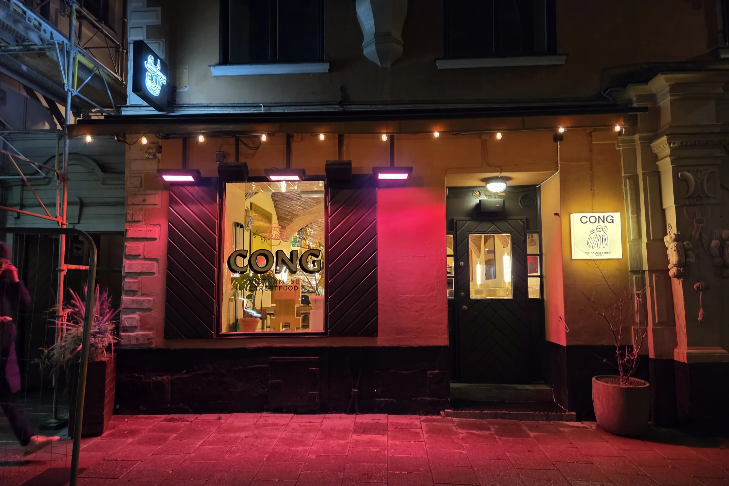 The front entrance to restaurant Cong, illuminated at night with pink light and the window showing the inside of the restaurant.